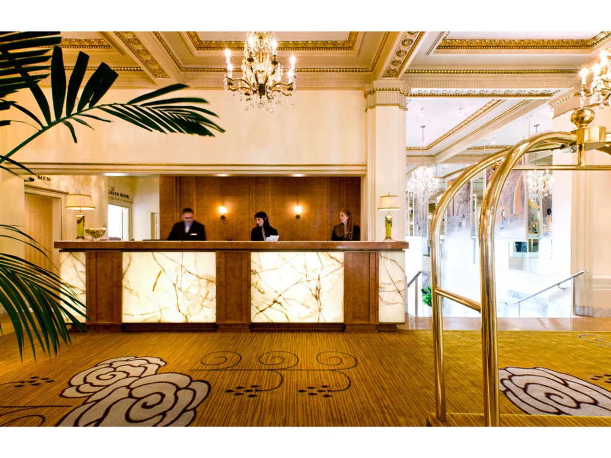 The reception area features a well-appointed front desk with attentive staff, a sparkling chandelier overhead, and a decorative carpet, setting the tone for impeccable service and ease upon arrival.