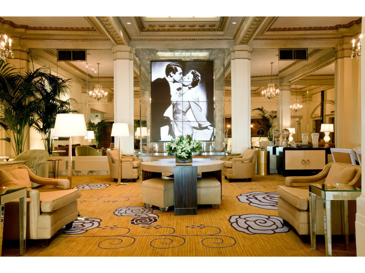 A chic seating area centered around a round table with a floral arrangement, comfortable chairs, and a striking large black and white art piece on the wall. The space feels both artistic and welcoming, with soft lighting that accentuates elegance.