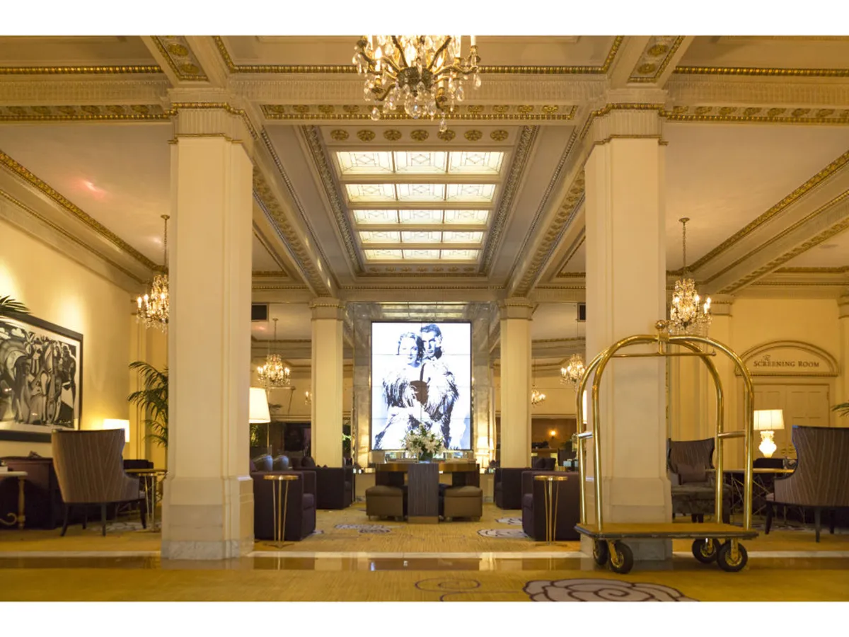 This image captures a sophisticated lobby setting with elegant chandeliers, striking artwork, and comfortable seating areas. The lively scene suggests guests relaxing, socializing, and enjoying refreshments, embodying the boutique hotel ambiance and welcoming atmosphere.