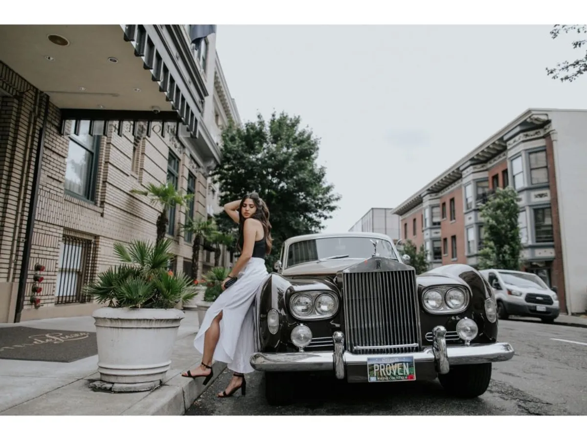 A chic exterior scene with a classic car, a woman in elegant attire, and the lush greenery along the street. The building’s facade is visible, and the atmosphere feels both luxurious and inviting, suggesting easy access to both the hotel and the surrounding neighborhood.